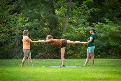 3 women in legband shorts - 2 are helping the 3rd do warrior pose